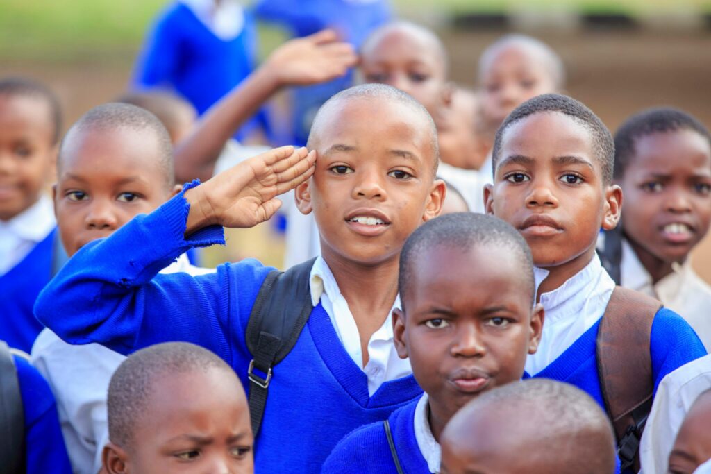 A group of school children in blue uniforms saluting outdoors on a sunny day.
