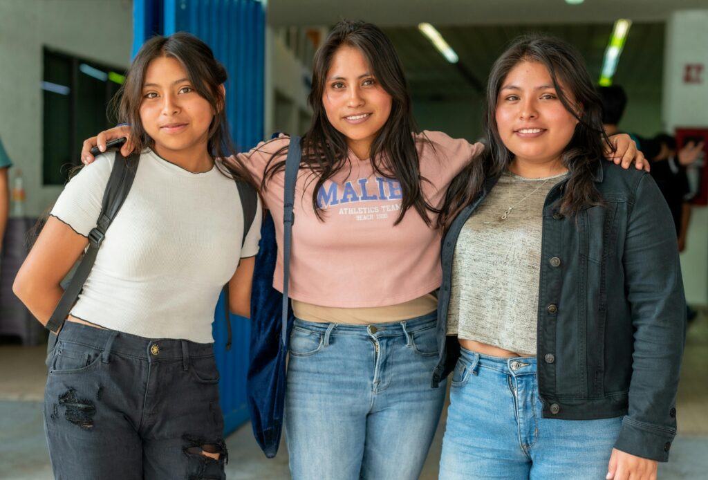 Three young women stand outdoors, smiling and hugging, dressed in casual outfits. Perfect for friendship and lifestyle themes.
