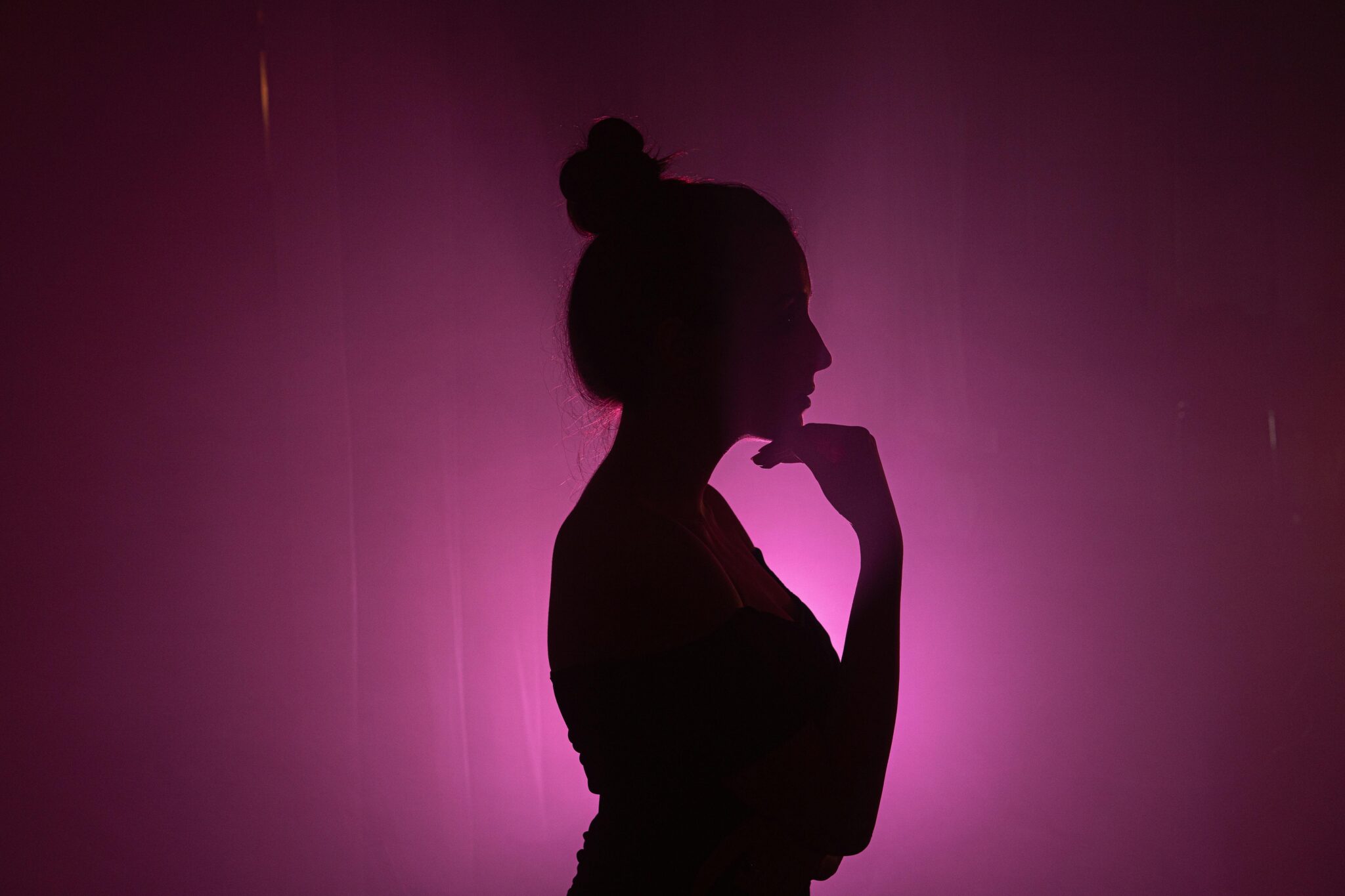 Artistic silhouette of a woman with long hair against a vibrant pink background.