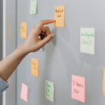Person organizing colorful sticky notes on a glass wall in an office setting.