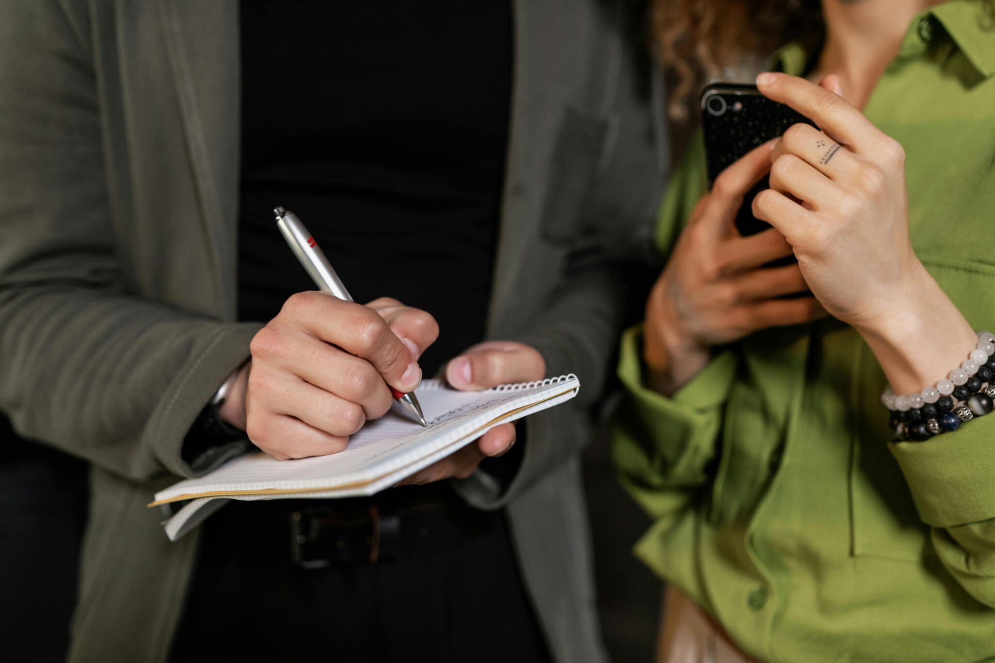 Two hands, one writing in a notebook, the other holding a smartphone, captured close-up.