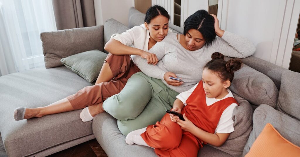 A mother, daughter, and family friend enjoy quality time together on a living room sofa.