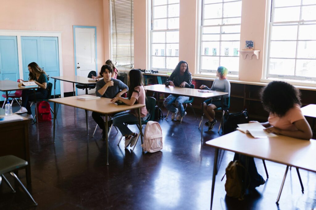 A diverse group of students interacting and studying in a classroom with large windows.