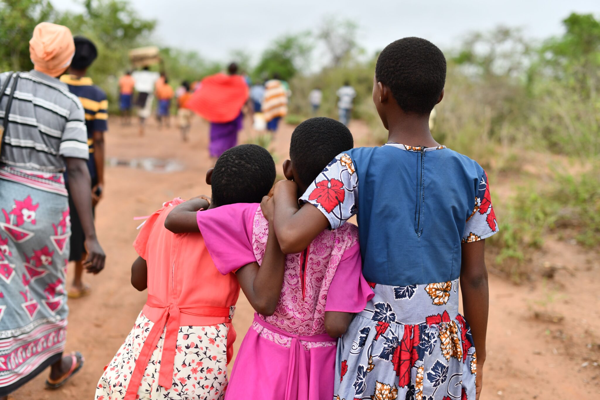 Three children embracing while walking on a dirt road, showcasing friendship and unity.