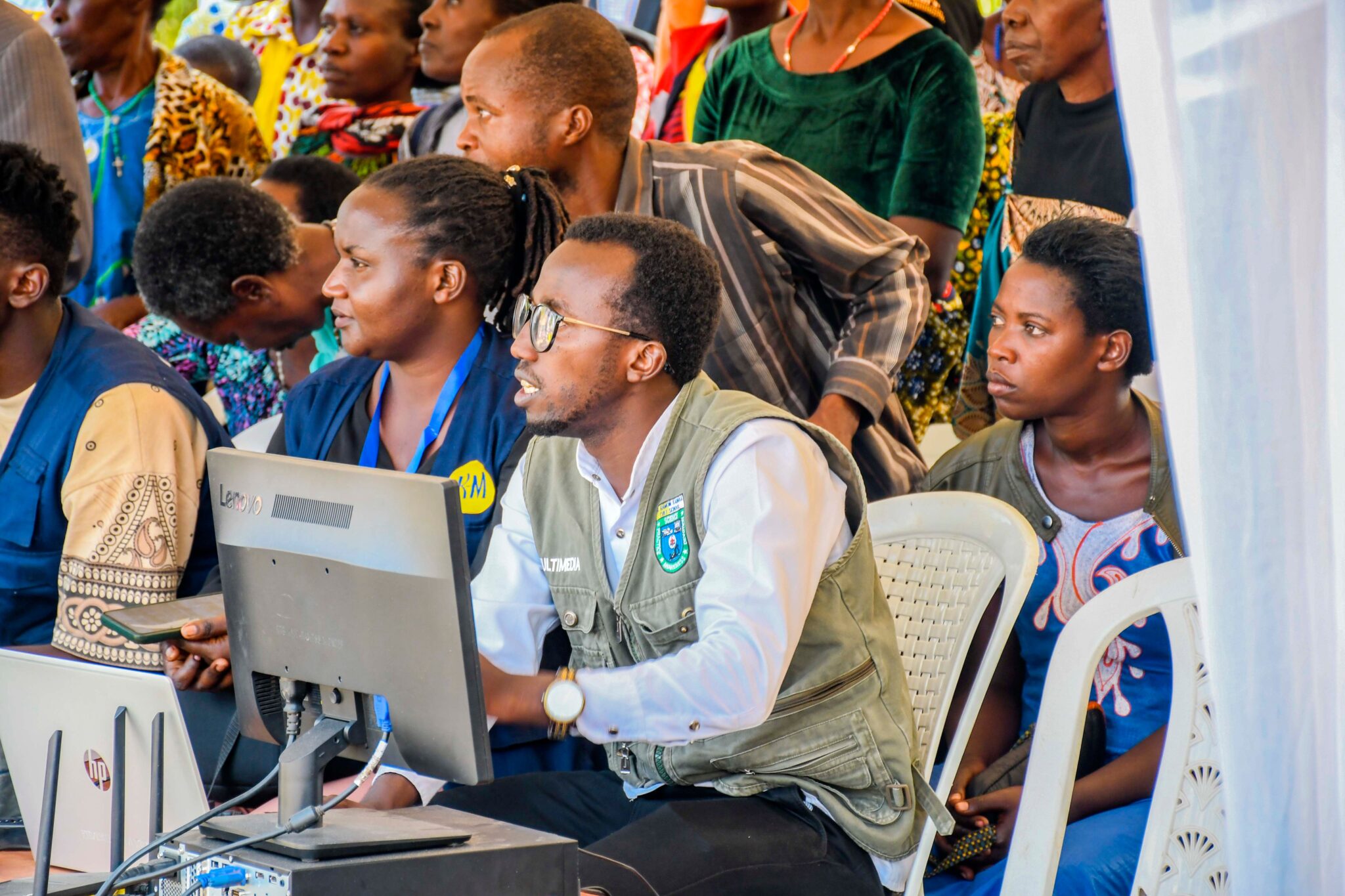 Build the Base A diverse group of adults engaging with technology at a community event in Rwanda.