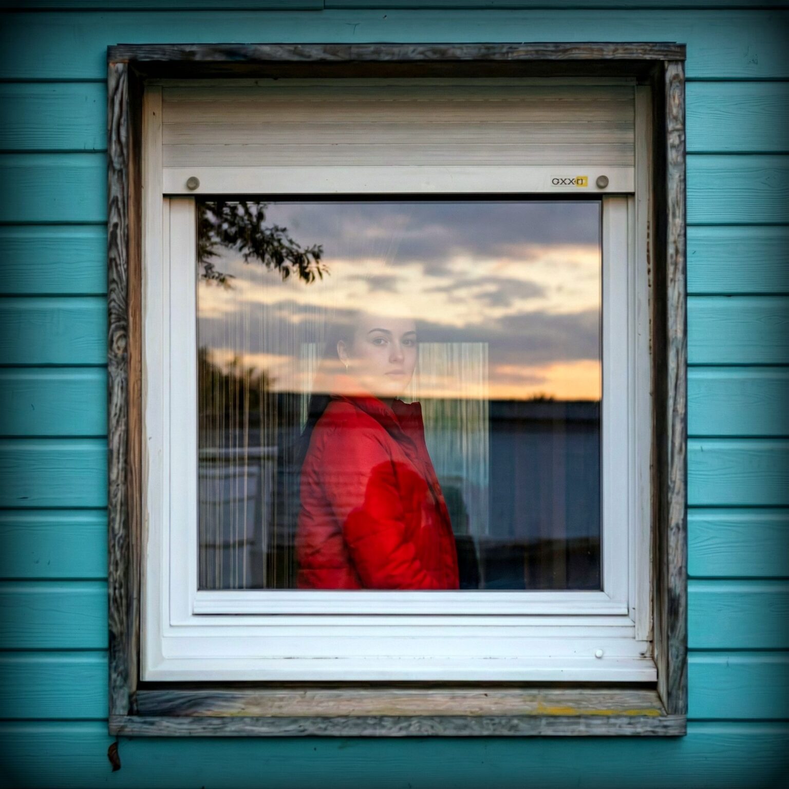 HopeWorks VITAL Captivating portrait of a person in a red jacket by a window, reflecting sunset hues.