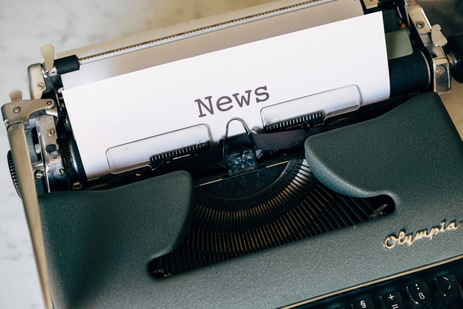 Impact & Insights Close-up of a vintage Olympia typewriter with paper reading 'news'. Perfect for classic journalism themes.