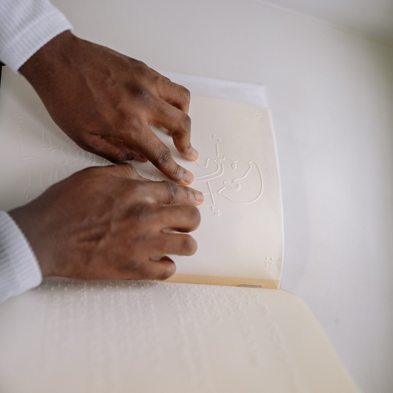 HopeWorks VITAL Close-up of hands reading a Braille book, symbolizing literacy for the visually impaired.